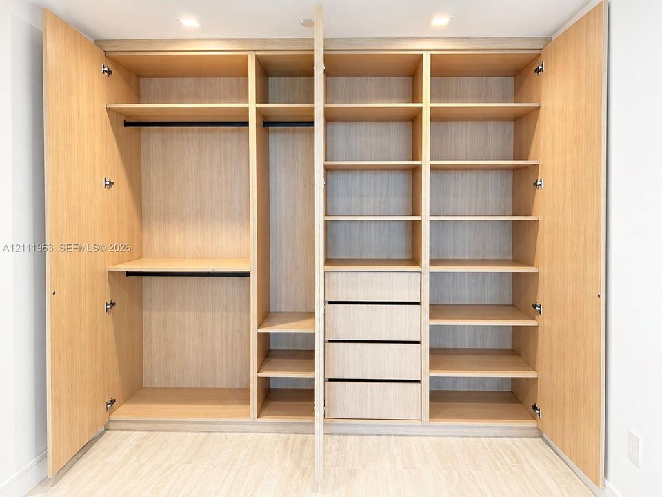 Custom-built light wood-finish storage cabinetry featuring integrated shelving, four stacked drawers, and dual hanging rods