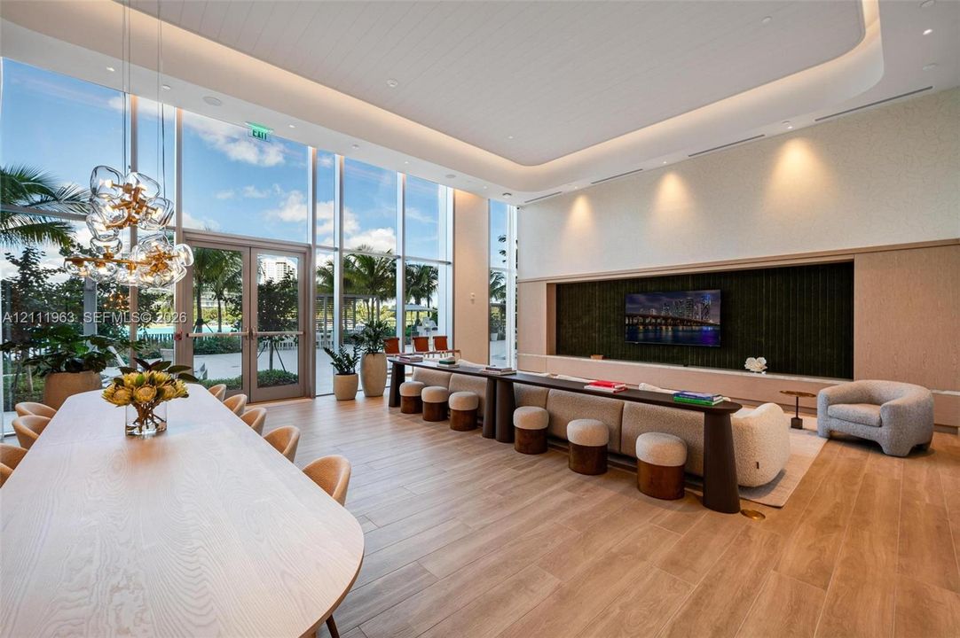 Floor-to-ceiling glass windows, wood-finish flooring, recessed tray ceiling with integrated lighting, custom built-in media wall with inset display, and sculptural multi-bulb pendant lighting