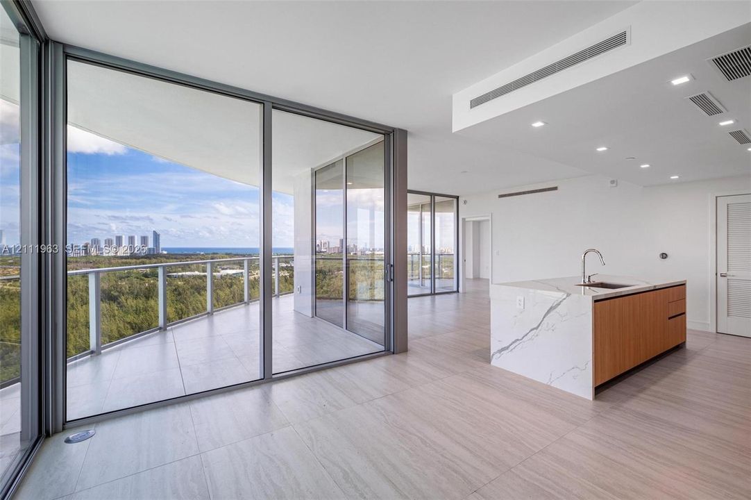 Floor-to-ceiling glass walls, expansive wraparound terrace with metal railings, kitchen island featuring waterfall-edge stone countertop, wood-finish cabinetry, and large-format tile flooring