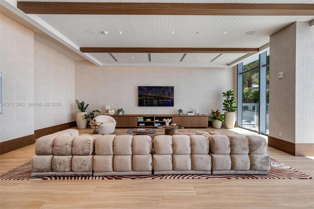 Living area featuring wood-finish flooring, ceiling with exposed beams, recessed lighting, built-in wooden cabinetry, and floor-to-ceiling glass wall panels
