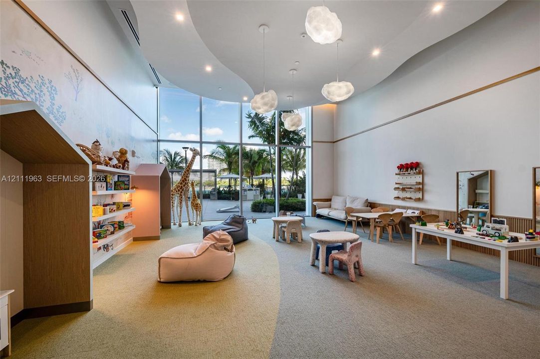 Expansive room featuring floor-to-ceiling windows, custom built-in wood shelving, intricate tray ceiling detail, recessed lighting, and sculptural pendant fixtures