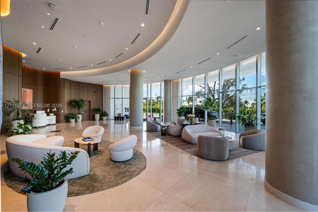 Grand lobby featuring floor-to-ceiling glass walls, curved architectural ceiling detailing, polished stone flooring, and warm-toned wood-finish wall paneling
