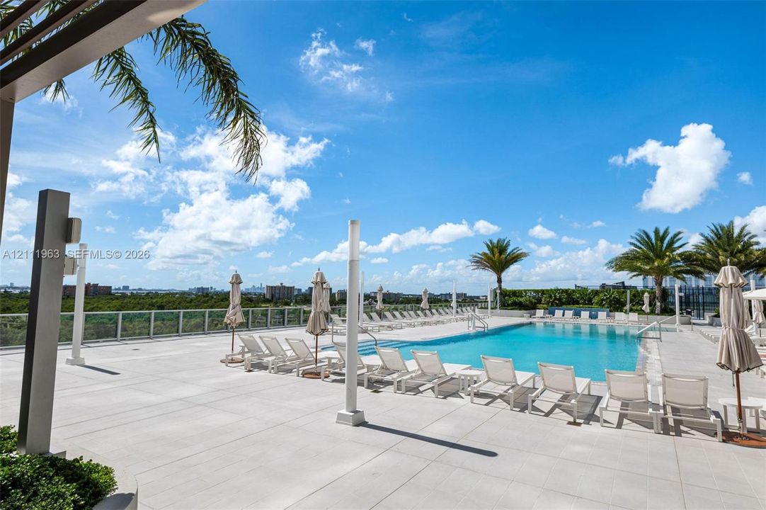 Rooftop pool featuring a paved deck, glass panel perimeter railing, and integrated overhead pergola structure