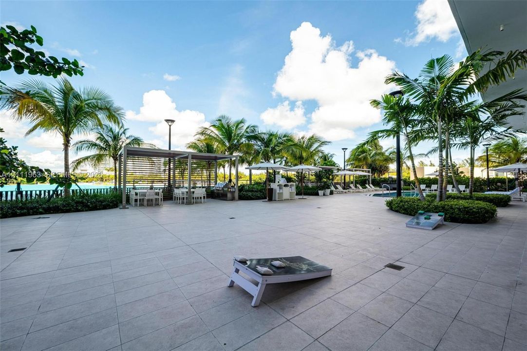 Expansive stone-paved patio featuring a covered pergola, built-in outdoor kitchen, integrated landscape lighting, and mature palm trees