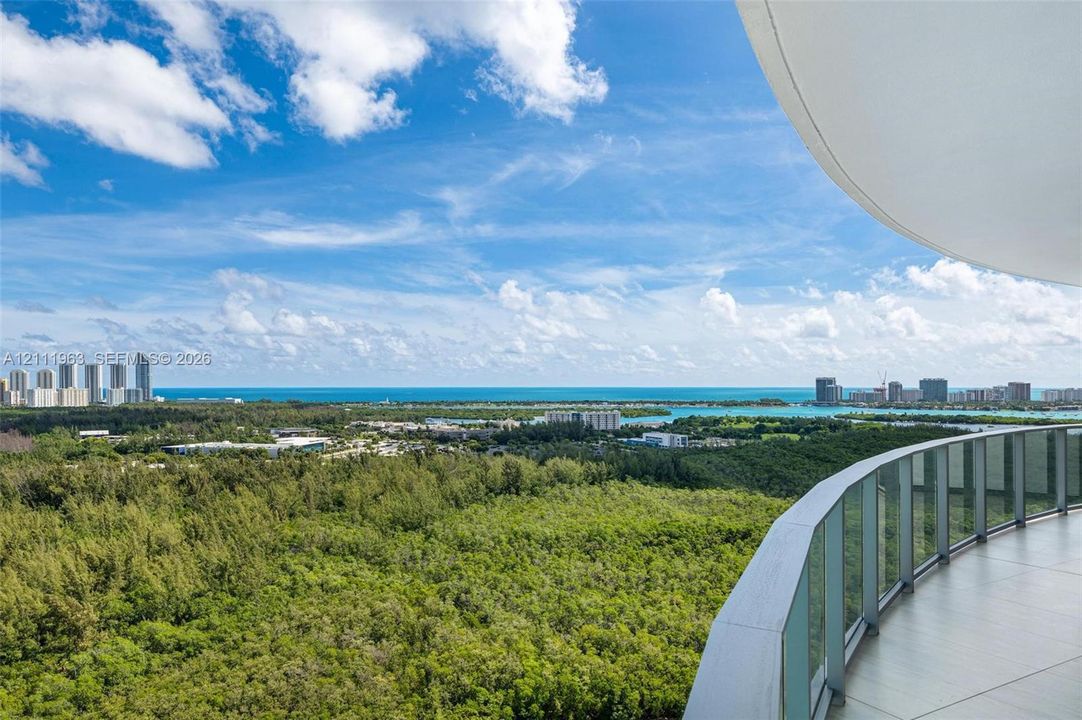 Curved balcony featuring large-format tile flooring and a glass panel railing, showcasing an expansive coastal and forested landscape
