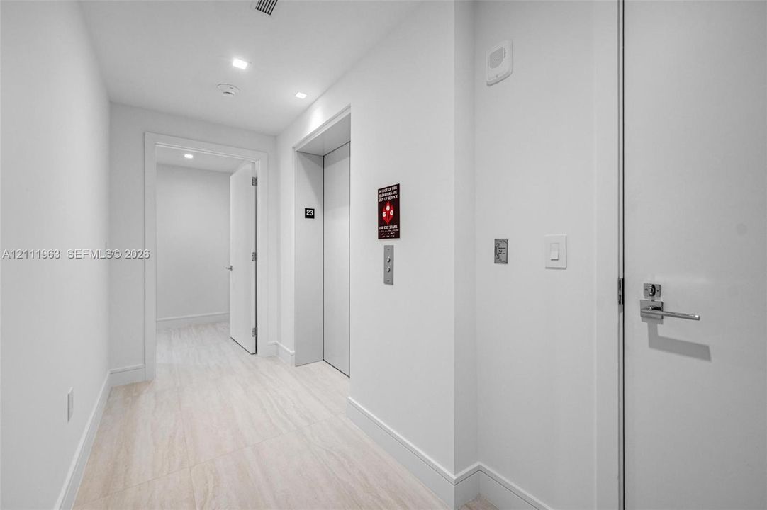Hallway featuring neutral-toned stone-finish flooring, recessed ceiling lighting, and dedicated elevator access