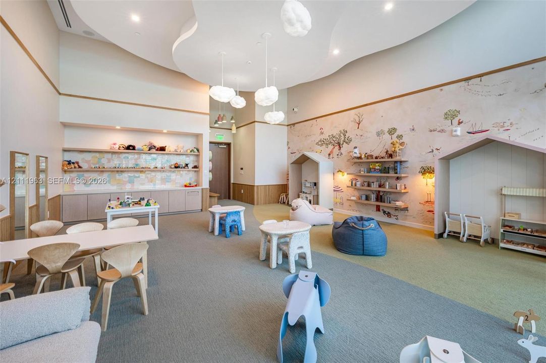 High-ceilinged room featuring a sculpted tray ceiling with pendant lighting, custom built-in cabinetry with integrated shelving, house-shaped architectural wall alcoves, and a decorative mural wall
