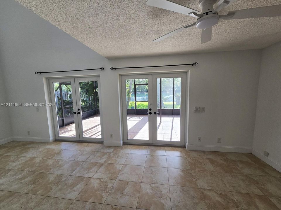 Vaulted ceilings featuring a white finish, neutral-toned tile flooring, dual sets of glass-paned double doors, and a ceiling-mounted light fixture with a fan