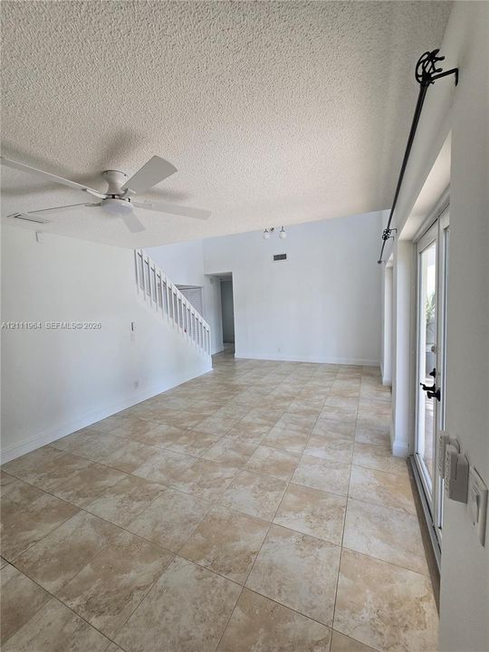 Open living area featuring vaulted ceilings, neutral tile flooring, a white staircase with wooden balusters, a ceiling fan, and double glass-panel doors