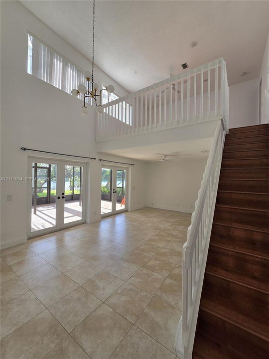 Two-story ceiling height with a multi-light chandelier, staircase with wood-finish treads and white balusters, large-format tile flooring, and dual sets of glass-paned doors