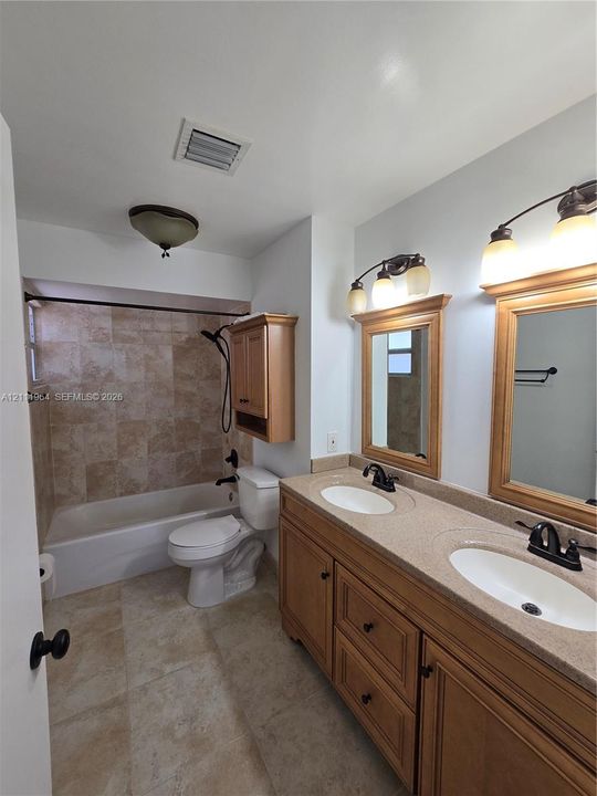 Double vanity featuring a stone-composite countertop, dual undermount sinks, wood-finish cabinetry, and framed mirrors, complemented by a tub-shower combination with tiled surround and matching tile flooring