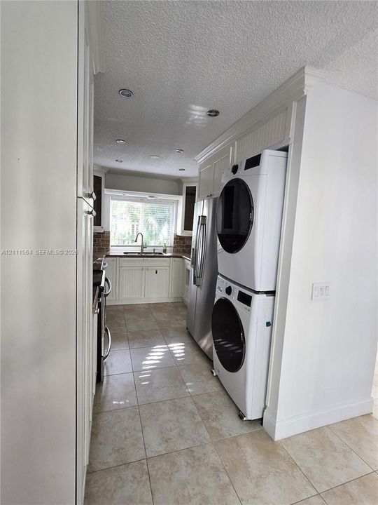 Kitchen featuring white beadboard cabinetry, recessed ceiling lighting, tile flooring, and integrated laundry appliances