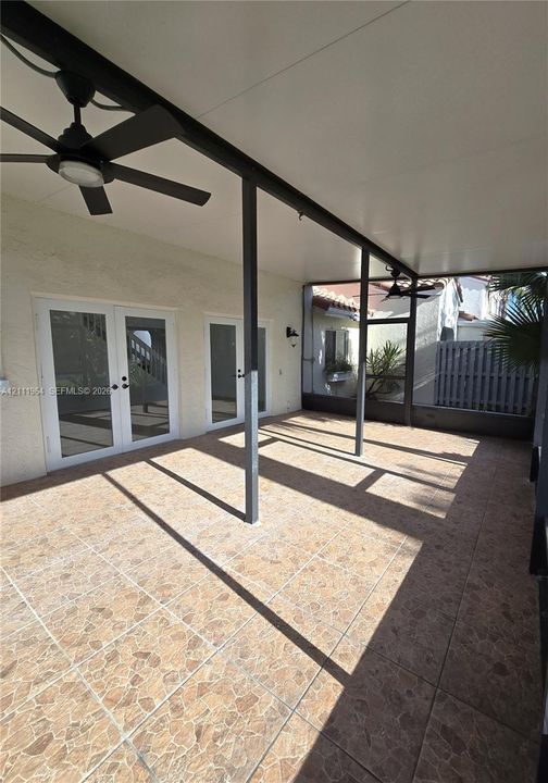 Covered patio featuring stone-tile flooring, dual ceiling fans, and screened-in enclosure with double French doors