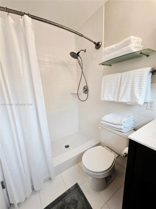 Shower enclosure featuring white wall tile, a handheld shower fixture, built-in soap niche, and a wall-mounted glass shelf