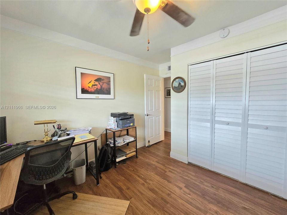 Room featuring wood-finish flooring, white louvered-style closet doors, a ceiling fan with integrated lighting, and crown molding