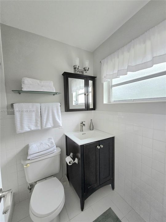 Dark-finish wooden vanity with a white countertop and integrated sink, complemented by a matching mirrored medicine cabinet, a wall-mounted glass shelf, and classic white tiled wall surfaces