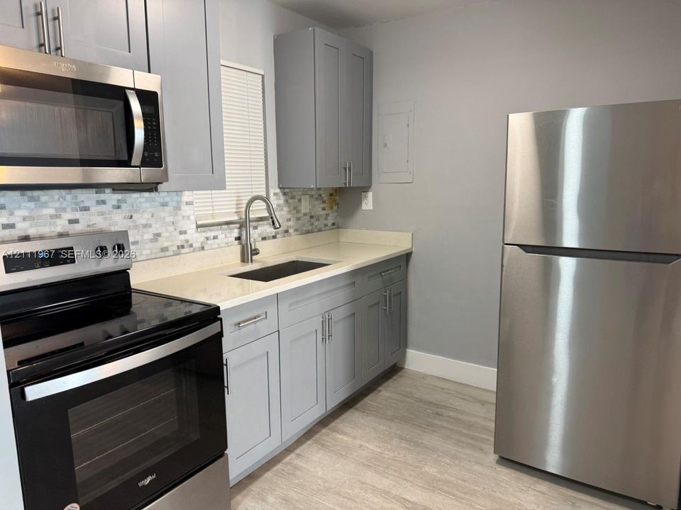 Kitchen featuring stainless steel appliances, grey shaker-style cabinetry, solid-surface countertops, mosaic tile backsplash, and wood-finish flooring