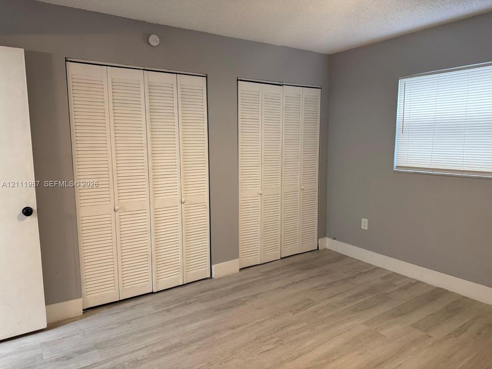 Wood-finish flooring, two sets of white louvered-door closets, and a window with integrated blinds
