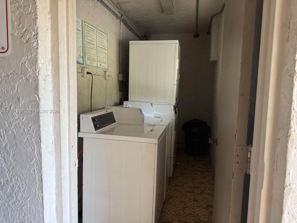 Laundry area featuring a top-load washing machine and a stacked dryer unit, accompanied by patterned resilient flooring and textured wall finishes