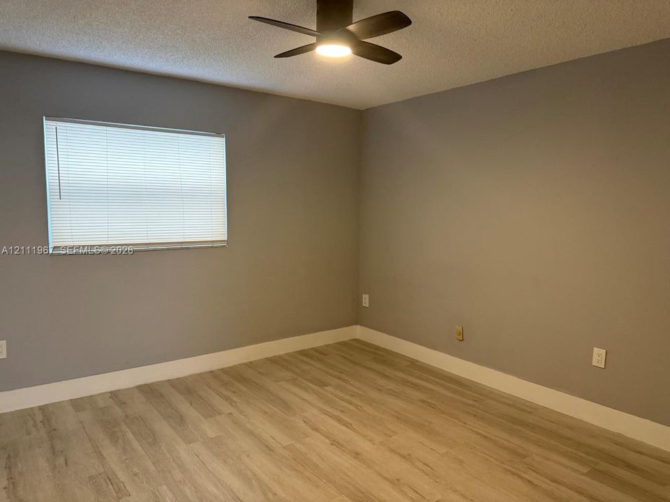 Interior room featuring wood-finish flooring, neutral-toned walls, and a multi-blade ceiling fan with integrated light