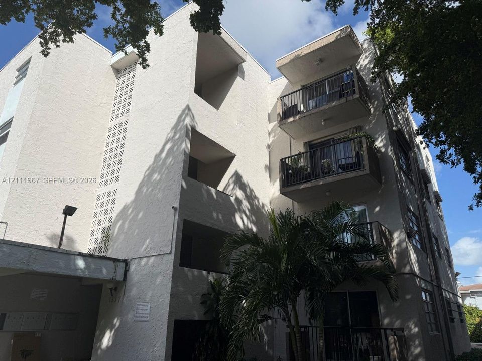 Multi-level exterior featuring a stucco facade, decorative breeze block accents, private balconies with metal railings, and a covered ground-level entryway