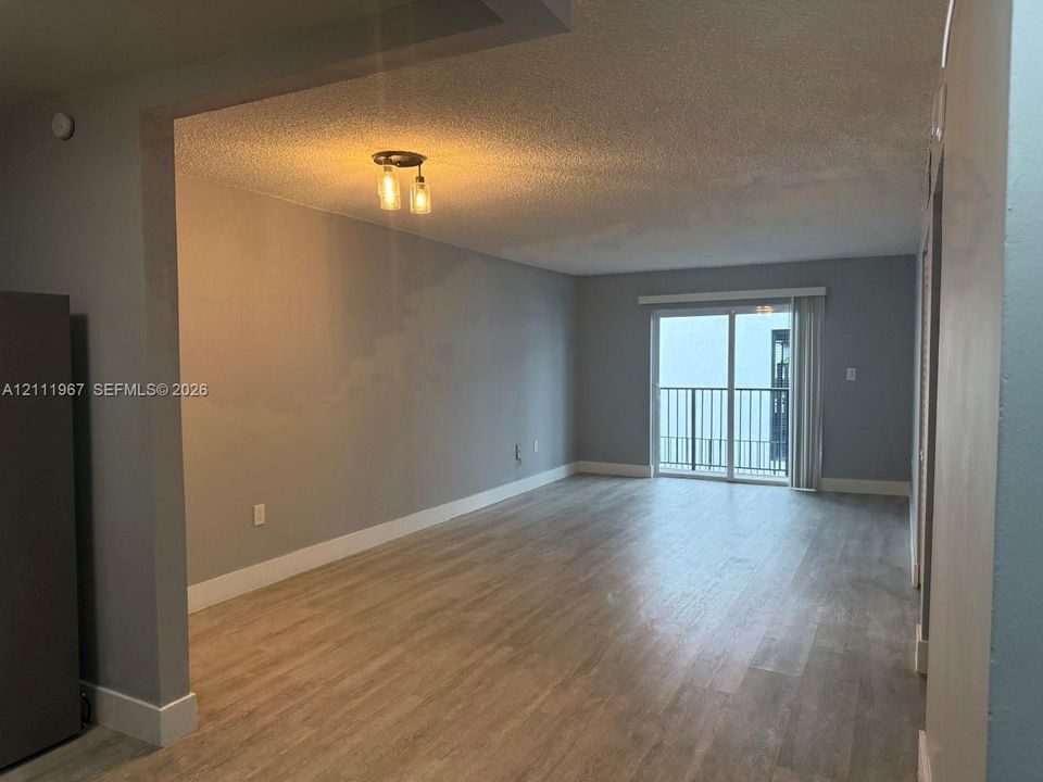 Open-concept interior featuring wood-finish flooring, a three-light pendant fixture, and a sliding glass door providing external access to a balcony with metal railings