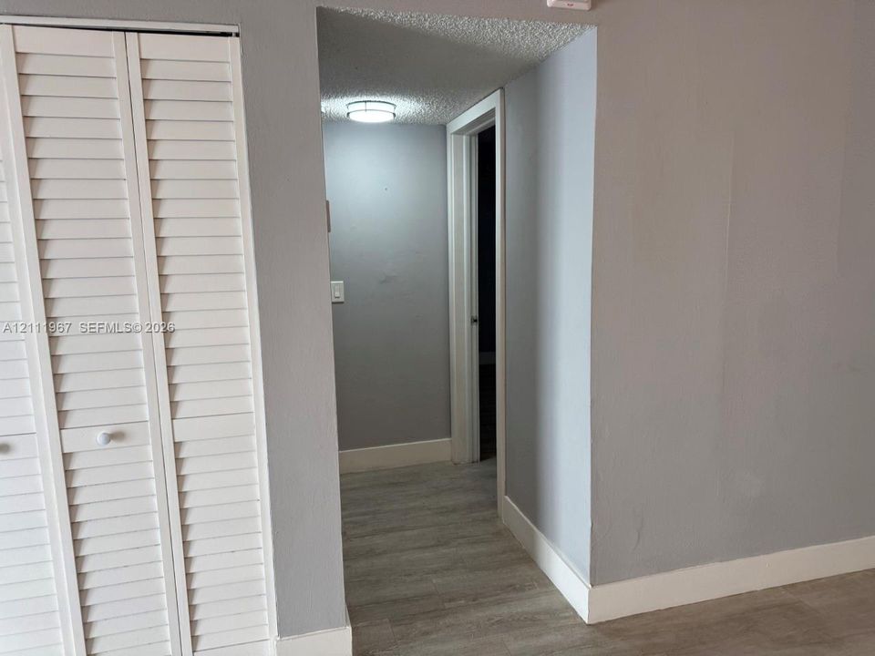 White louvered-style closet doors, neutral grey wall paint, wood-finish flooring, and a flush-mount circular ceiling light fixture