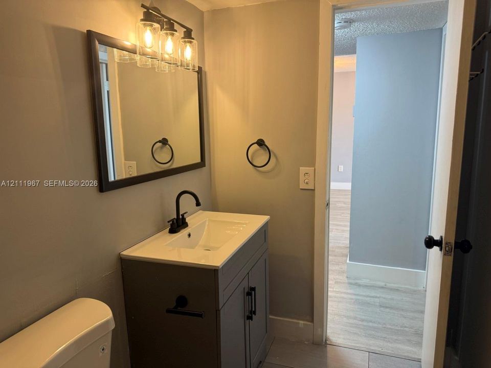 Gray vanity cabinet with a white countertop, rectangular integrated sink, matte black faucet, wall-mounted three-light fixture, and framed mirror