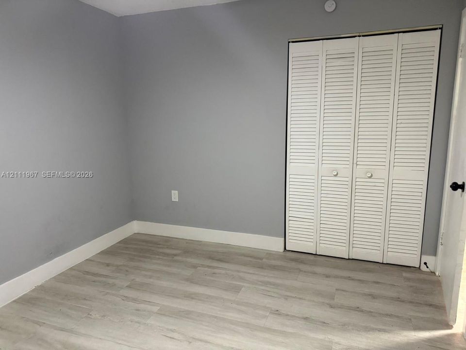Interior room featuring grey walls, wood-finish flooring, and white louvered bifold closet doors