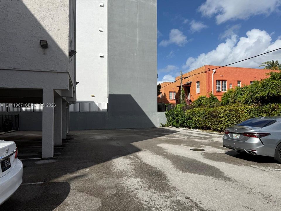 Asphalt parking area featuring covered parking spaces and metal perimeter fencing