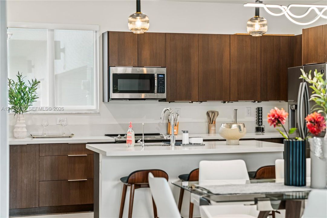 Kitchen featuring dark-stained flat-panel cabinetry, stone countertops, a central island with an integrated sink, stainless steel microwave, and glass globe pendant lighting