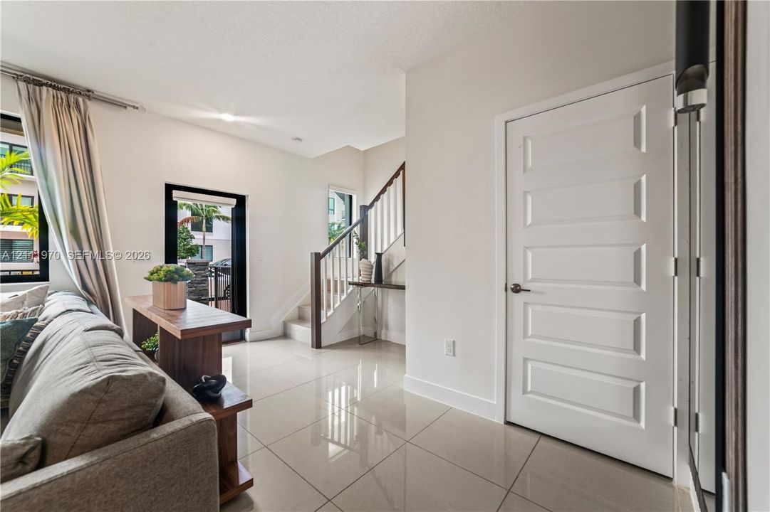 Interior featuring large-format tile flooring, five-panel interior door, and staircase with dark wood handrail and white balusters
