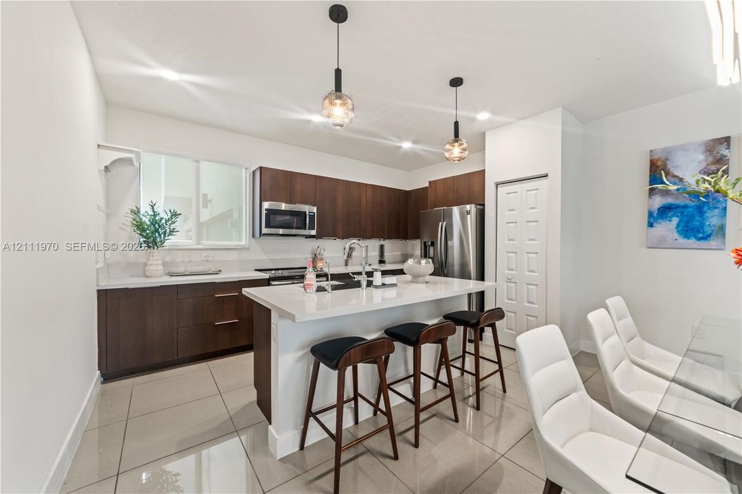 Kitchen featuring dark wood-finish cabinetry, a white stone-surface island, stainless steel appliances, large-format tile flooring, and dual pendant light fixtures