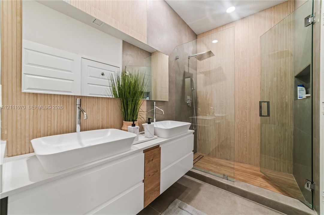 Modern dual-vanity featuring white vessel sinks, quartz countertops, wood-accent cabinetry, floor-to-ceiling vertical wood-finish wall paneling, and a walk-in glass-enclosed shower with integrated recessed shelving