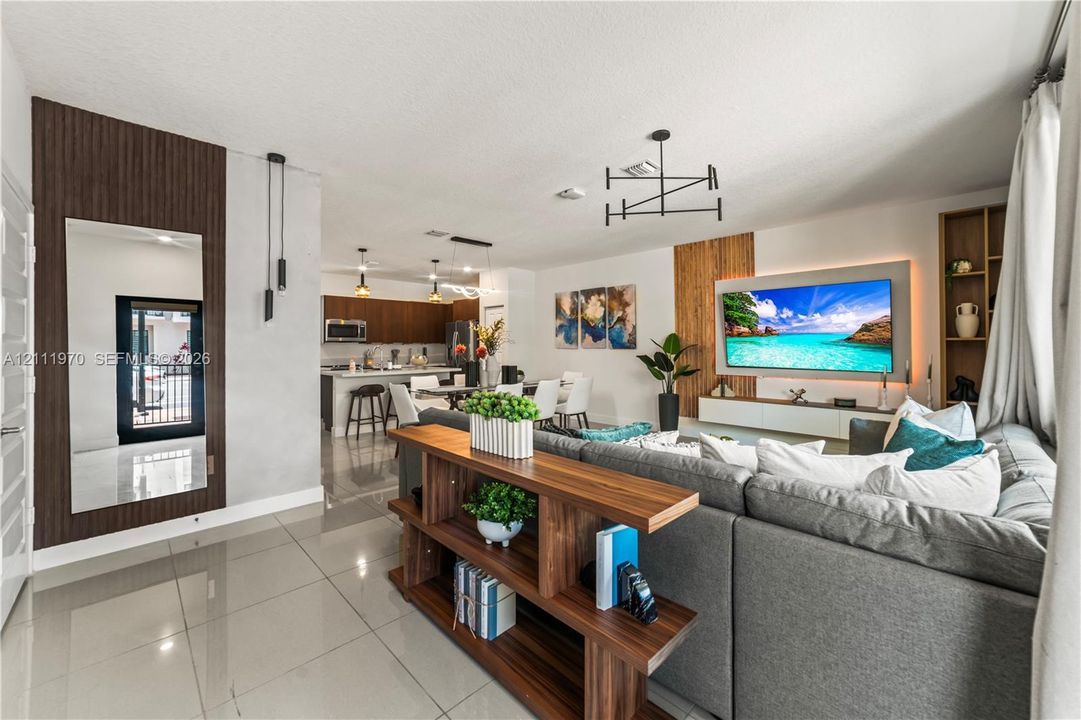 Open-concept interior featuring large-format tile flooring, vertical wood-slat wall accents, contemporary multi-arm light fixtures, a built-in media console with integrated recessed lighting, and floor-to-ceiling mirror paneling