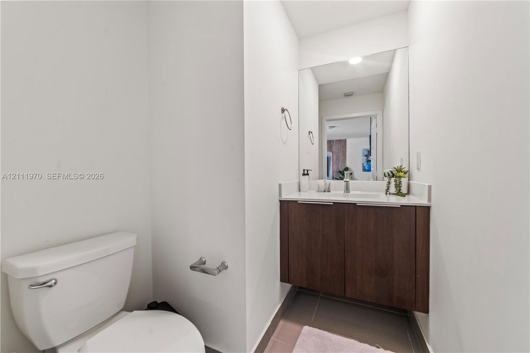 Floating vanity featuring dark wood-finish cabinetry, a rectangular sink with a single-handle faucet, a solid-surface countertop, and a large-format frameless mirror