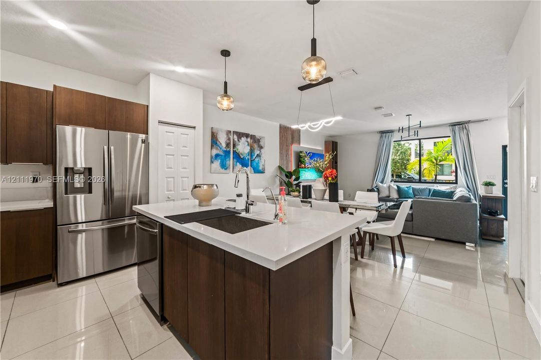 Kitchen featuring a central island with a quartz countertop, stainless steel refrigerator, dark wood-finish cabinetry, polished tile flooring, and decorative pendant lighting