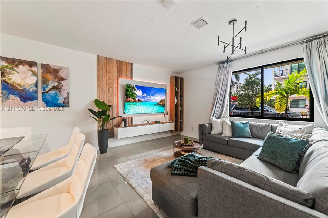 Living area featuring neutral-toned tile flooring, custom vertical wood slat accent wall, minimalist floating media console with integrated cabinetry, and geometric multi-arm chandelier