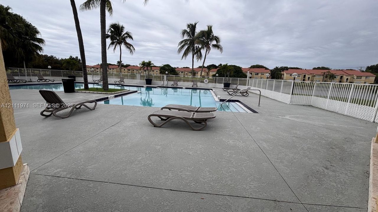 Swimming pool area featuring a concrete deck, metal perimeter fencing, and mature palm trees