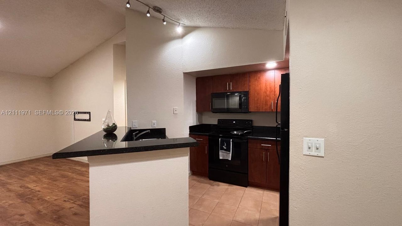 Kitchen featuring dark-toned cabinetry, solid surface countertops, black appliances, tile flooring, and vaulted ceilings with track lighting