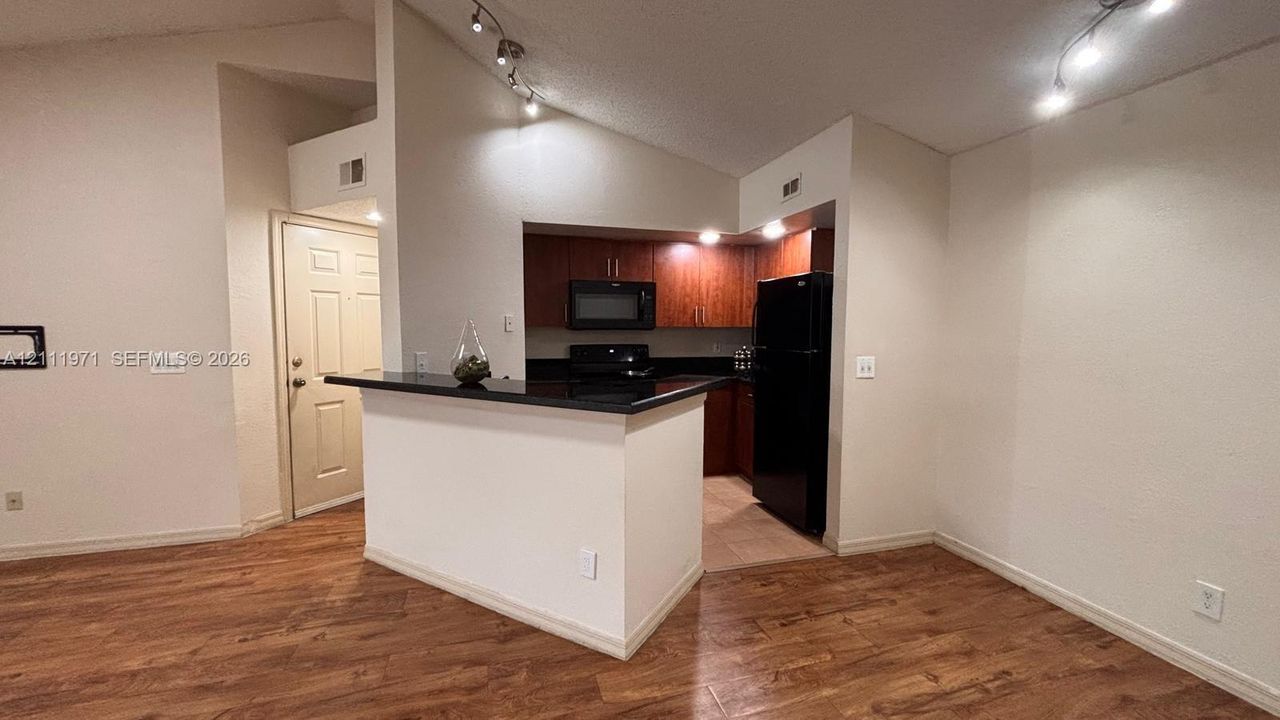 Kitchen featuring wood-finish cabinetry, black countertops, a breakfast bar, and vaulted ceilings with track lighting