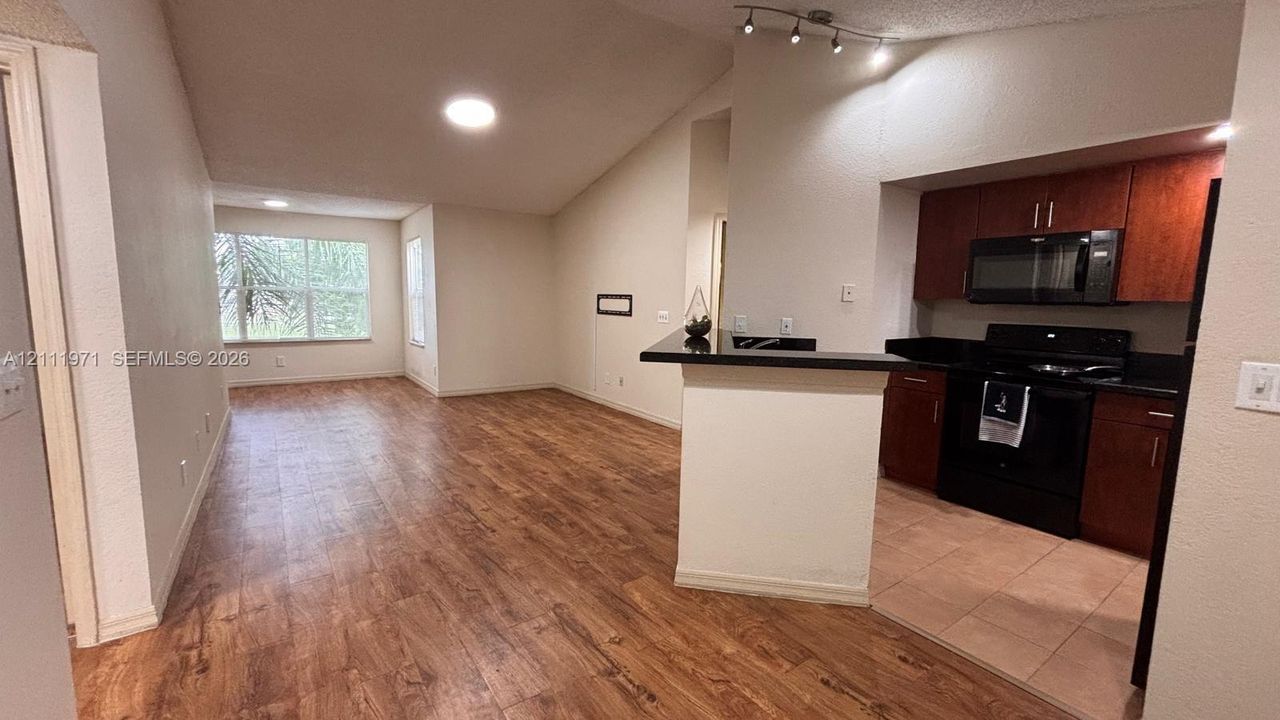 Vaulted ceilings, wood-finish flooring, dark-toned cabinetry, breakfast bar with stone-surface countertop, and ceramic tile kitchen flooring