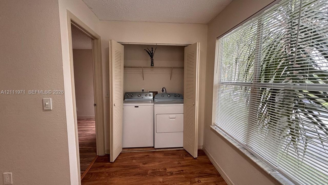 Laundry area featuring dual louvered closet doors, integrated shelving, and wood-finish flooring
