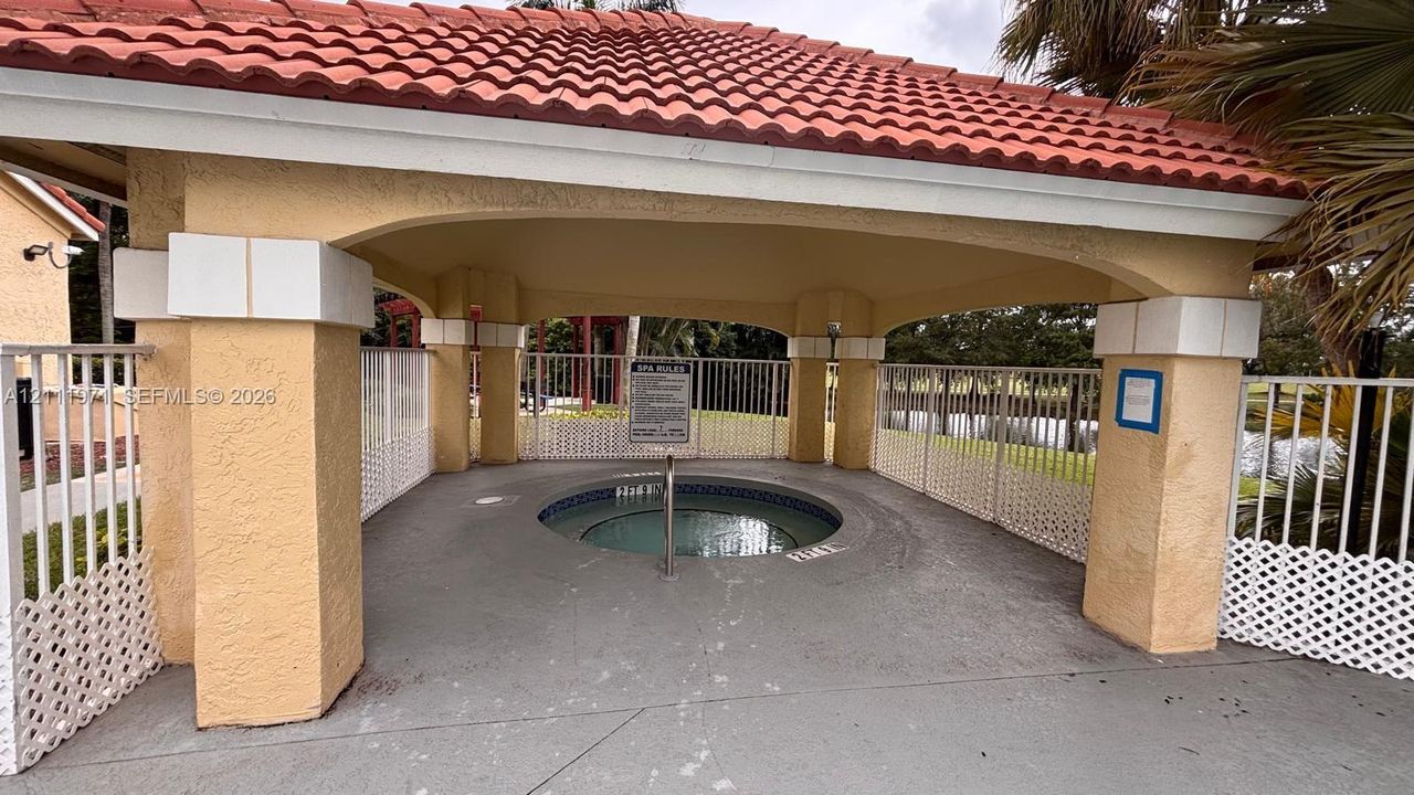 Covered spa area featuring a terracotta tile roof, structural stucco columns, and metal perimeter fencing
