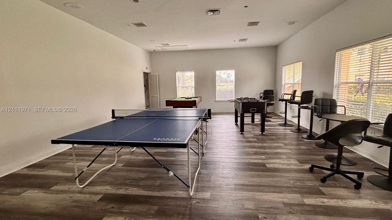Open-concept recreation area featuring wood-finish flooring, recessed lighting, and multiple windows with horizontal blinds