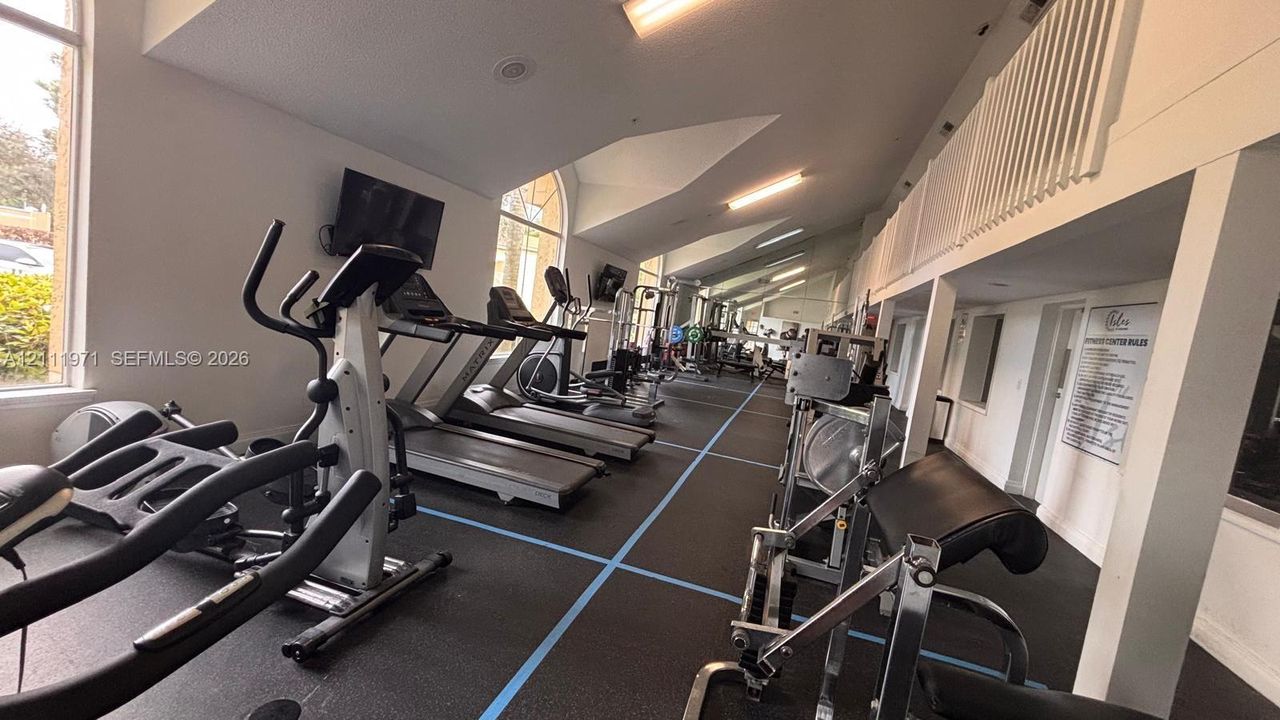 Fitness center featuring specialized rubberized flooring, vaulted ceilings, and expansive floor-to-ceiling windows