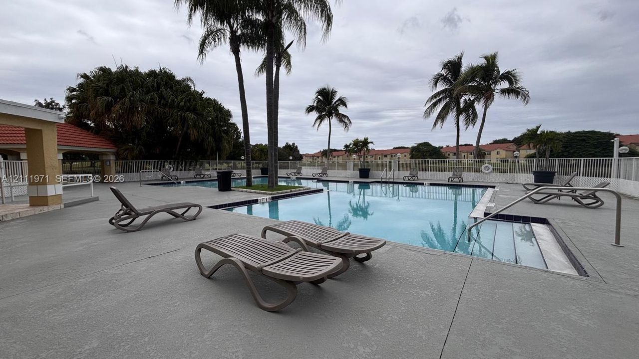 Swimming pool with a concrete pool deck, metal safety fencing, built-in stairs, and palm trees