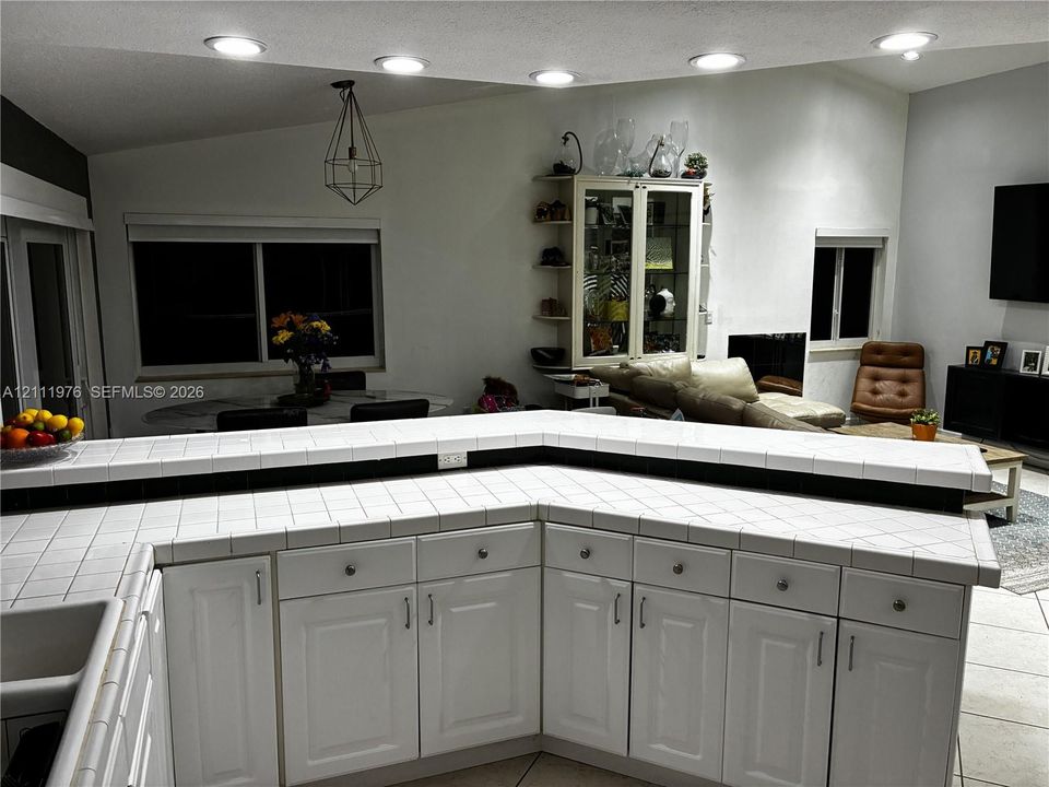 White cabinetry with shaker-style doors, tile countertops, built-in display shelving, recessed lighting, and a geometric pendant light fixture