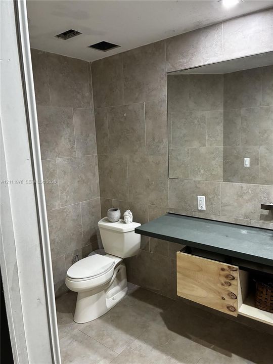 Bathroom featuring full-height large-format wall tiling, a floating vanity with a wood-finish cabinet, a dark-toned countertop, and a wall-to-wall mirror