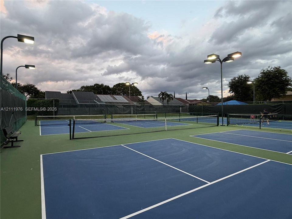Multi-court facility featuring hard-surfaced playing areas, perimeter fencing, and overhead court lighting